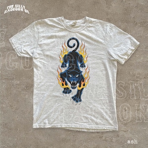 A white t-shirt with a graphic design depicting a black panther with flames surrounding it.