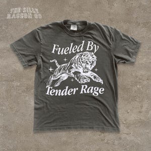 A gray t-shirt with a graphic design depicting a tiger and the text "Fuelled By Tender Rage" printed on it.