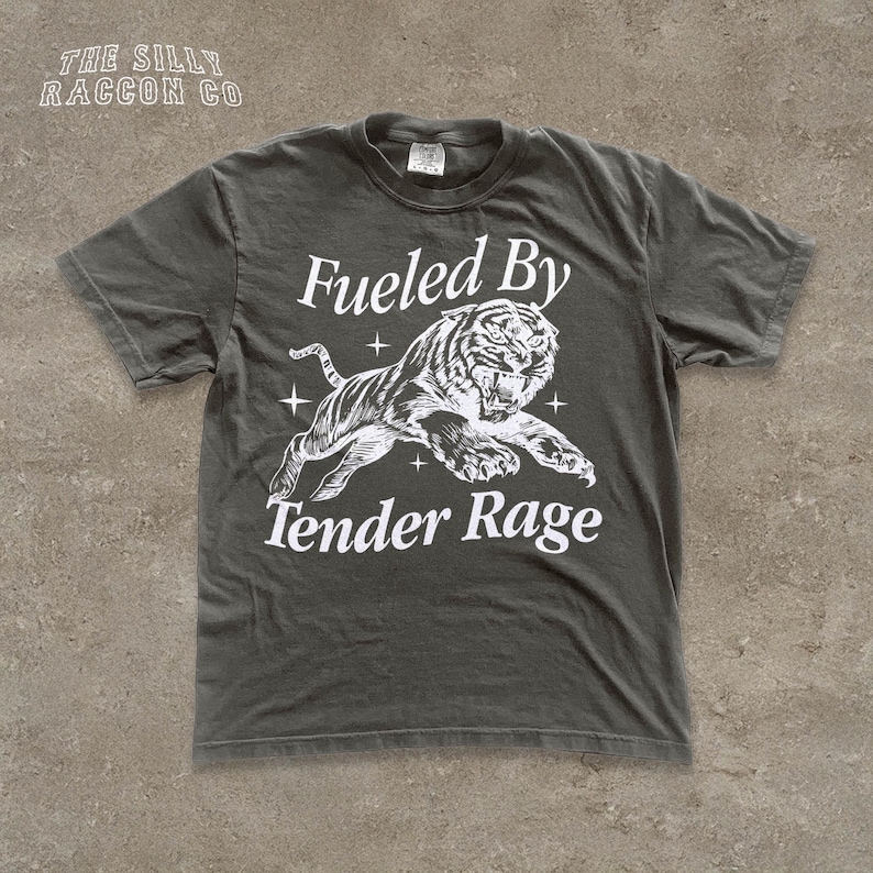 A gray t-shirt with a graphic design depicting a tiger and the text "Fuelled By Tender Rage" printed on it.