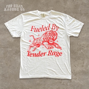 A white t-shirt with a graphic design featuring a tiger and the text "Fuelled By Tender Rage" printed on it.