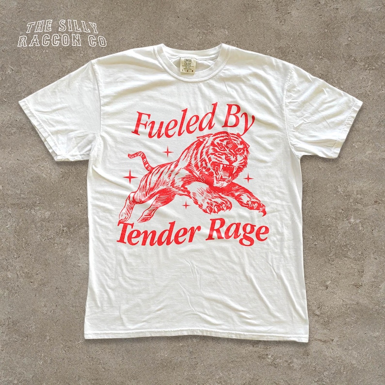 A white t-shirt with a graphic design featuring a tiger and the text "Fuelled By Tender Rage" printed on it.