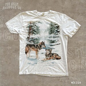 A white t-shirt with a printed design depicting two wolves in a snowy forest landscape.