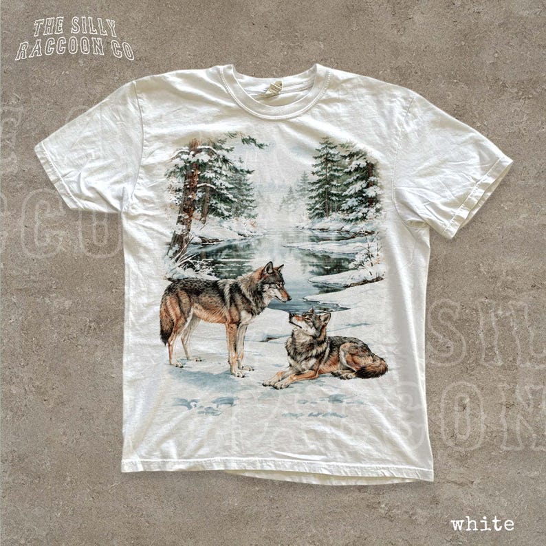 A white t-shirt with a printed design depicting two wolves in a snowy forest landscape.
