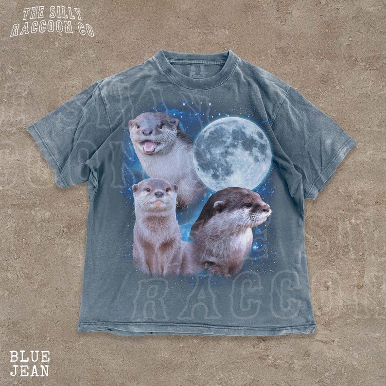 A t-shirt with a graphic design featuring three otters against a backdrop of a full moon and stars.