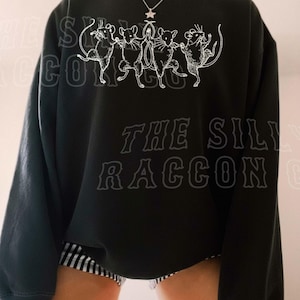 A person wearing a black sweatshirt with a graphic design featuring a group of cats.