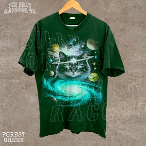 A green t-shirt with a cat wearing a helmet and surrounded by planets and a swirling galaxy design.