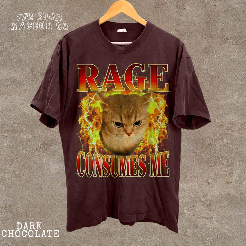 A dark brown t-shirt with a graphic design featuring a cat's face surrounded by flames and the text "RAGE CONSUMES ME" prominently displayed.