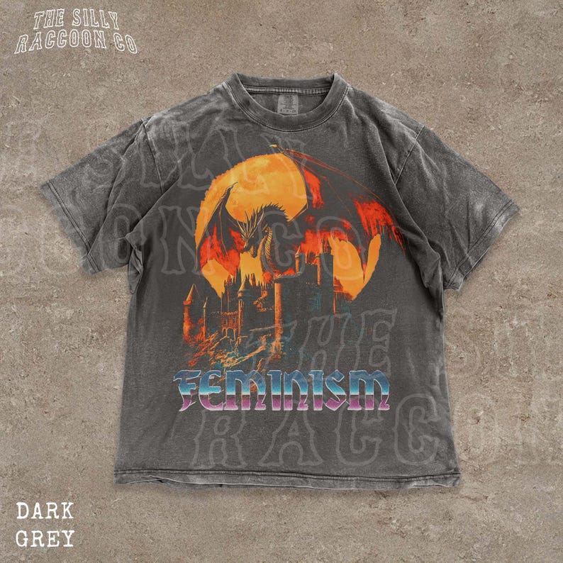 A grey t-shirt with a graphic design depicting a dragon and a castle, along with the word "Feminism" printed on it.