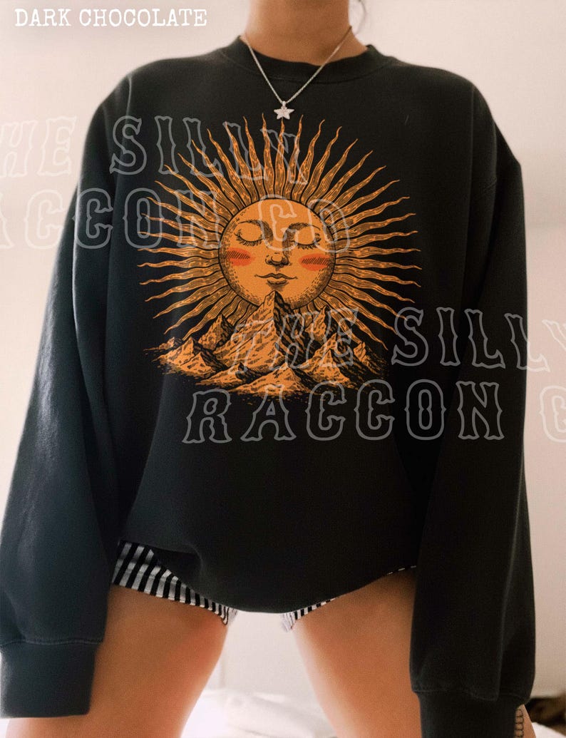 A person wearing a black sweatshirt with a sun design and mountains printed on it.