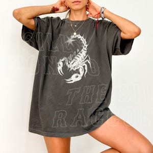A person wearing a gray t-shirt with a white graphic of a scorpion.