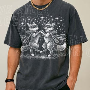 A man wearing a black t-shirt with a graphic design of two foxes dancing under a starry sky.