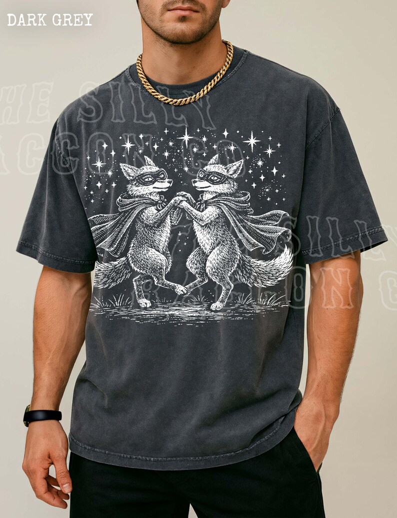 A man wearing a black t-shirt with a graphic design of two foxes dancing under a starry sky.