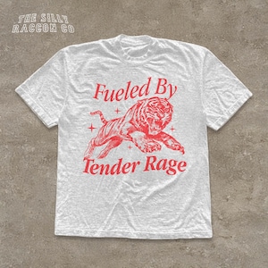 A white t-shirt with a red graphic design depicting a tiger and the text "Fuelled By Tender Rage" printed on it.