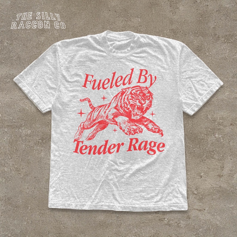 A white t-shirt with a red graphic design depicting a tiger and the text "Fuelled By Tender Rage" printed on it.
