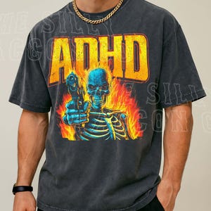 A man wearing a black t-shirt with a graphic design depicting a skeleton holding a gun and surrounded by flames.