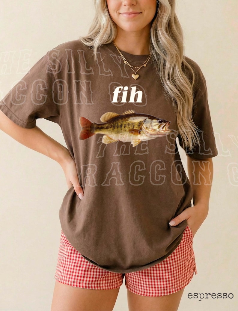 A woman wearing a brown t-shirt with a fish graphic and red and white shorts, smiling at the camera.