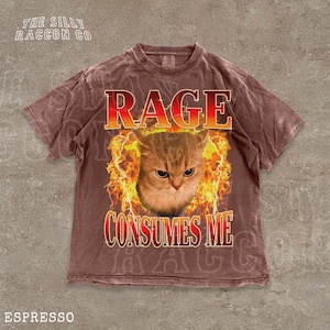 A t-shirt with a graphic design featuring a cat's face surrounded by flames, with the text "RAGE CONSUMES ME" prominently displayed.