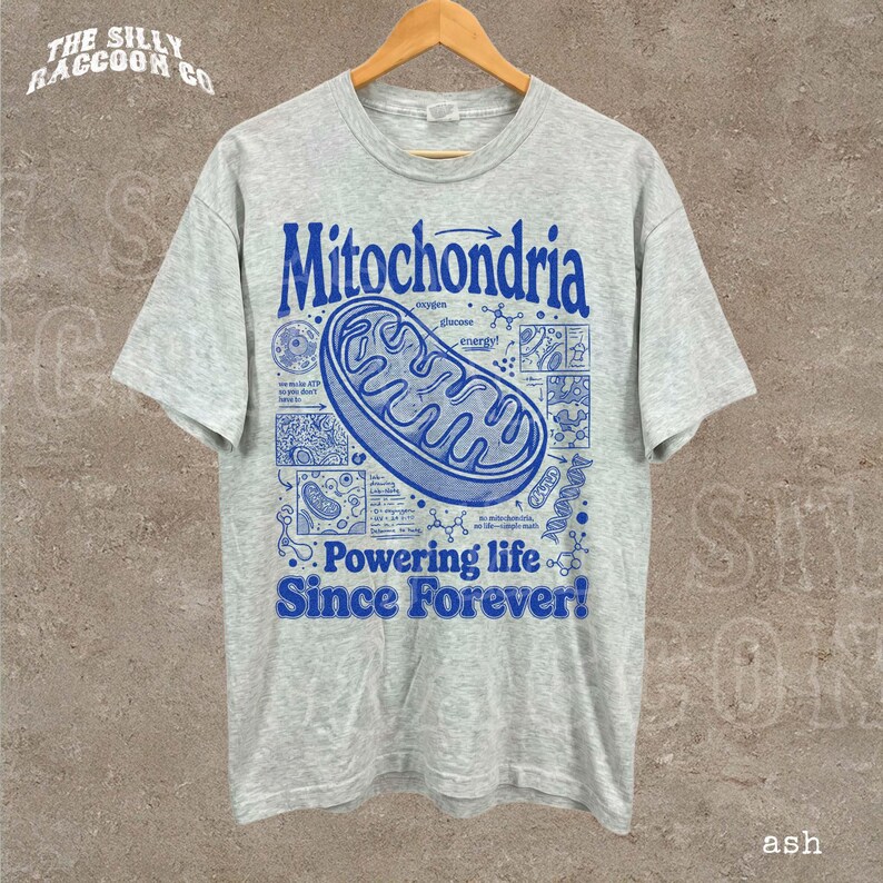 A gray t-shirt with a graphic design depicting a Mitochondria, a cellular organelle, and text that reads "Mitochondria - Powering life Since Forever!".