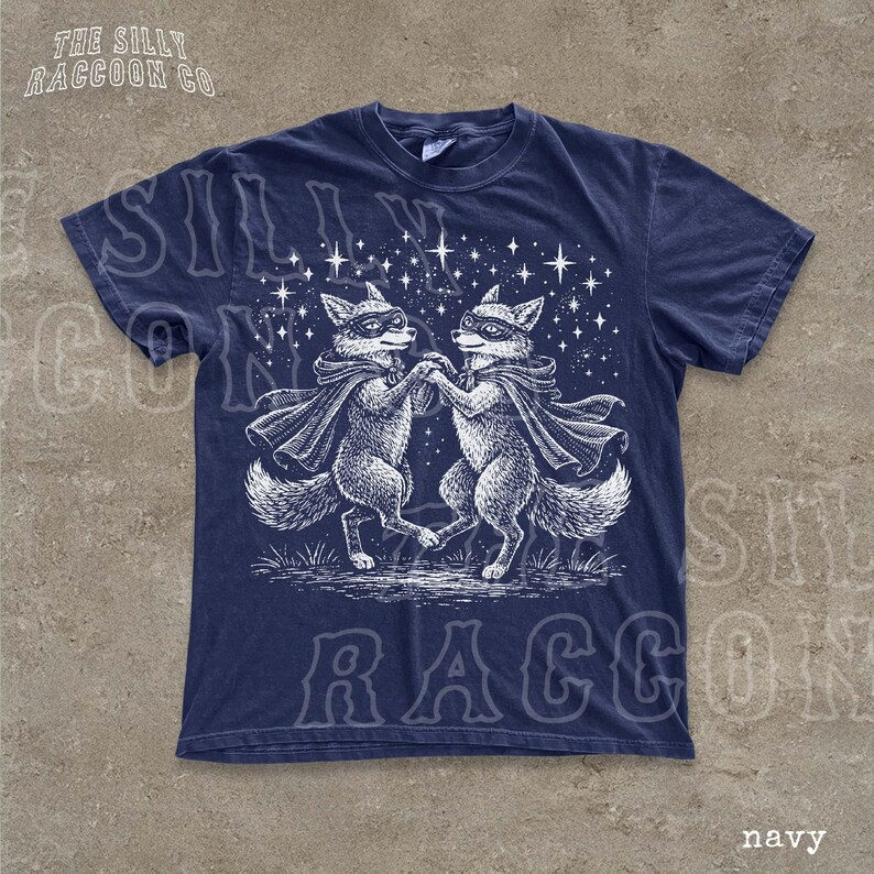 A navy blue t-shirt with a graphic design featuring two foxes dancing under a starry sky.