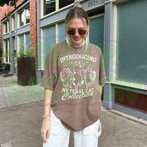 Vintage style feral cat collection t-shirt for cat moms, cat dads, and pet lovers featuring three playful red cat illustrations on a mint green background with sparkling stars. Retro-inspired graphic tee with "INTRODUCING MY FERAL CAT Collection" text in vintage typography perfect for cat rescue volunteers, animal lovers, veterinarians, and cat collectors.