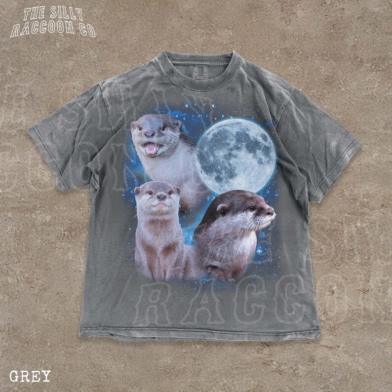 A grey t-shirt with a graphic design featuring three otters against a backdrop of a full moon and stars.