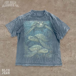 A blue t-shirt with a graphic design of three sea turtles swimming in the ocean.