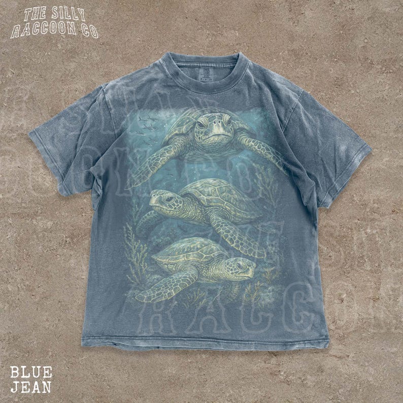 A blue t-shirt with a graphic design of three sea turtles swimming in the ocean.