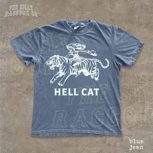 A blue t-shirt with a graphic design depicting a tiger and a person riding on its back, along with the text "HELL CAT" printed on it.