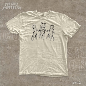 A white t-shirt with a graphic design depicting three cats with horns, each holding the other's tail.