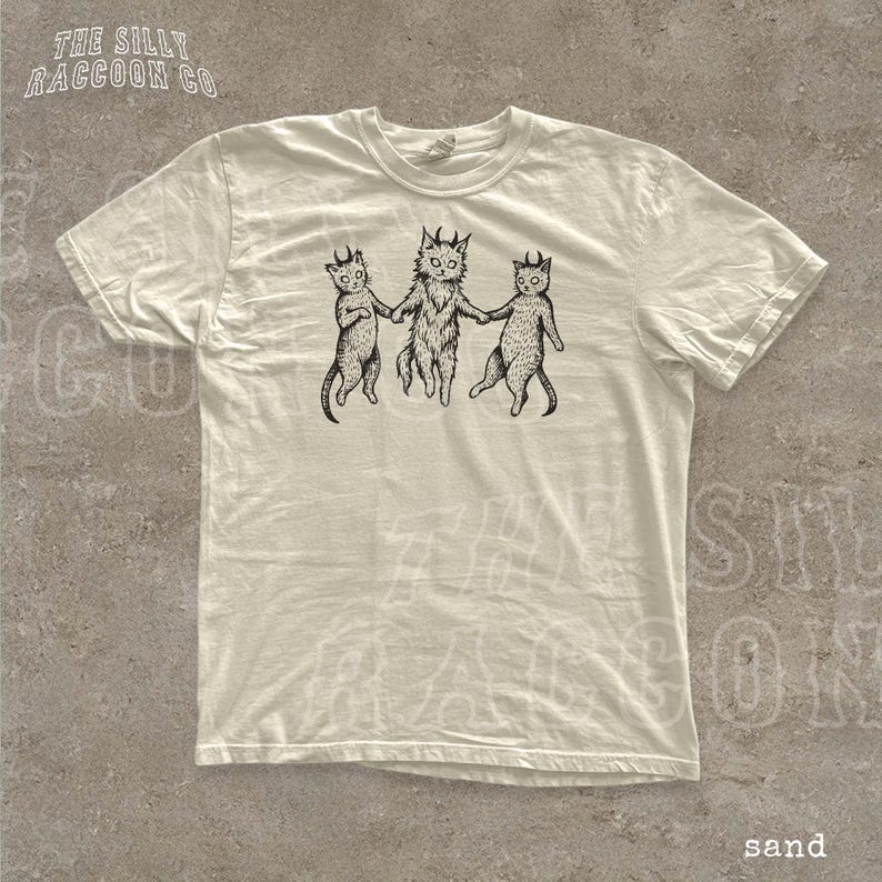 A white t-shirt with a graphic design depicting three cats with horns, each holding the other's tail.
