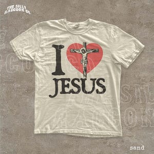 A white t-shirt with a graphic design featuring a red heart and the text "I I J E S" and "JESUS" printed on it.