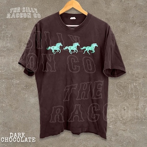 A dark brown t-shirt with a graphic design of three horses in motion, along with the text "THE SILLY RACCOON CO." printed on it.