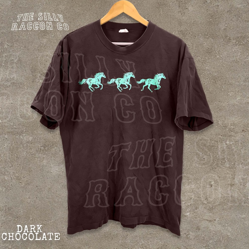 A dark brown t-shirt with a graphic design of three horses in motion, along with the text "THE SILLY RACCOON CO." printed on it.