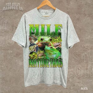 A grey t-shirt with a graphic design featuring a frog and the text "MILF MAN I LOVE FROGS" printed on it.