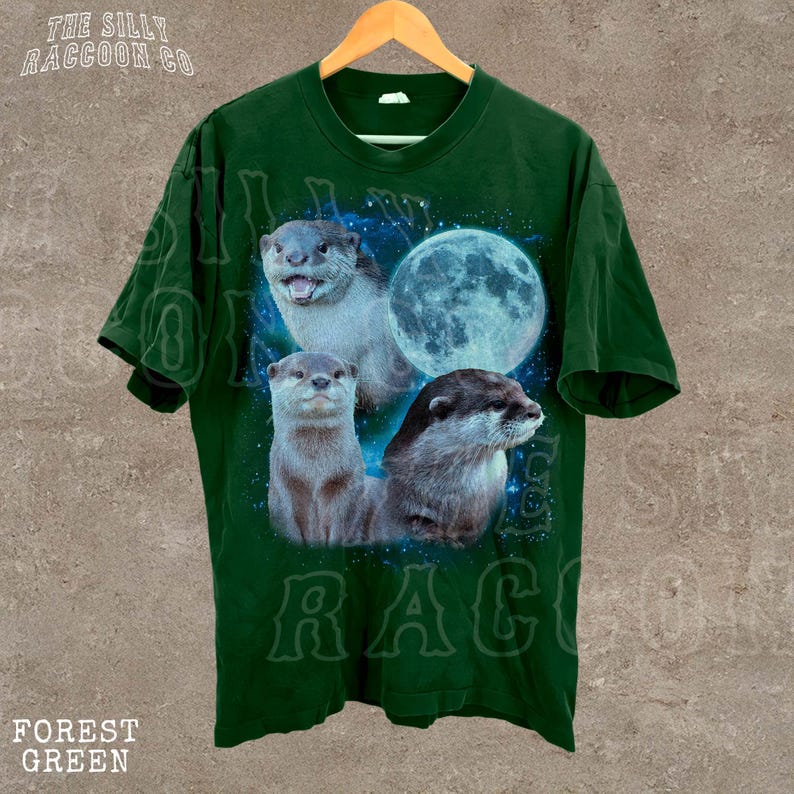 A green t-shirt with a graphic design featuring three otters against a backdrop of a full moon and stars.