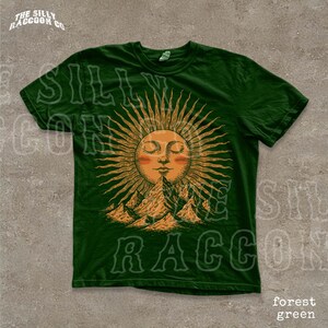 A green t-shirt with a sun design and mountains in the background.