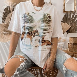 A person wearing a white t-shirt with a printed image of two wolves in a forest setting.