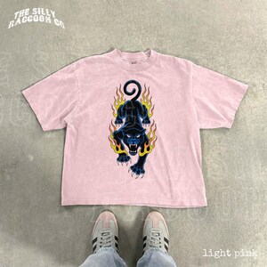 A pair of white sneakers and a pink t-shirt with a graphic design featuring a black panther with flames on its back.