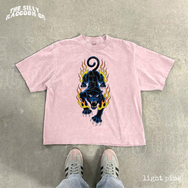A pair of white sneakers and a pink t-shirt with a graphic design featuring a black panther with flames on its back.