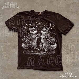 a black t-shirt with a graphic design depicting two foxes dancing together under a starry sky.