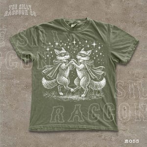 A green t-shirt with a white illustration of two foxes dancing under a starry sky.