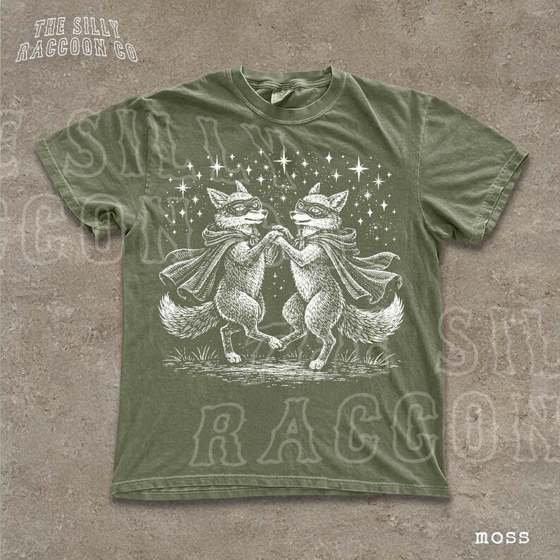 A green t-shirt with a white illustration of two foxes dancing under a starry sky.