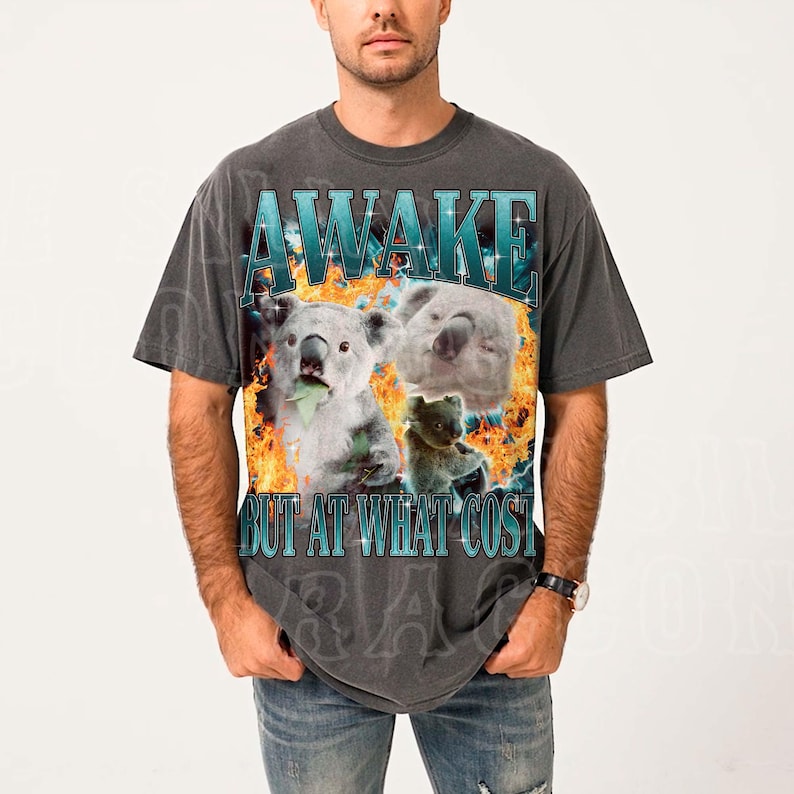 A man wearing a gray t-shirt with a graphic design featuring a koala and the text "A WAKE BUT AT WHAT COST".