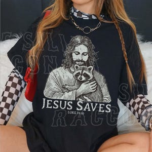 A person wearing a black t-shirt with a graphic of Jesus holding a raccoon.