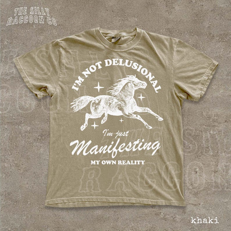 a t-shirt with a graphic design of a horse and the text "I'm not delusional, I'm just Manifesting, MY OWN REALITY" printed on it.