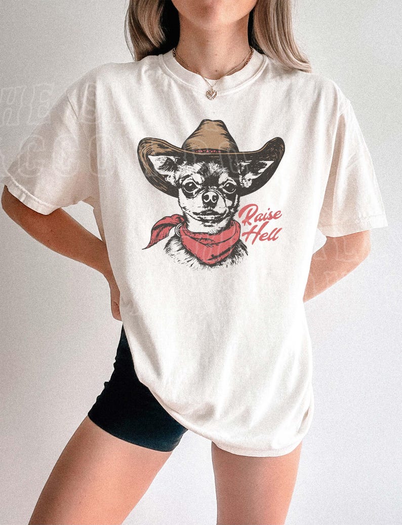 A woman wearing a white t-shirt with a graphic of a dog wearing a cowboy hat and a red scarf.