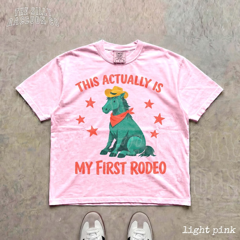 A pink t-shirt with a graphic of a green horse and the text "This actually is my first rodeo" printed on it.