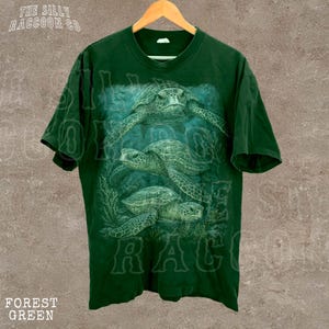 A green t-shirt with a printed design of three sea turtles swimming in the ocean.
