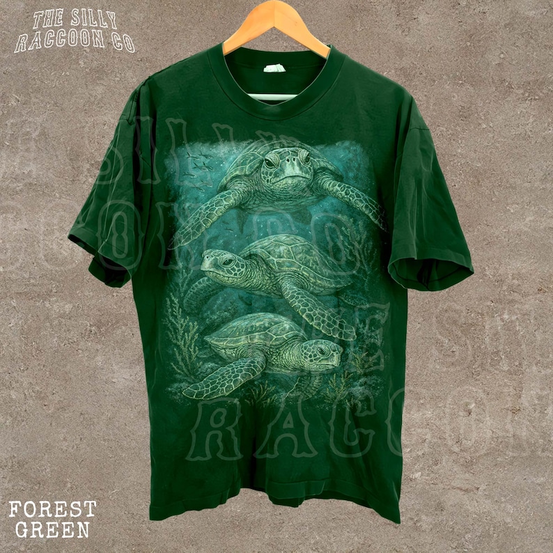 A green t-shirt with a printed design of three sea turtles swimming in the ocean.