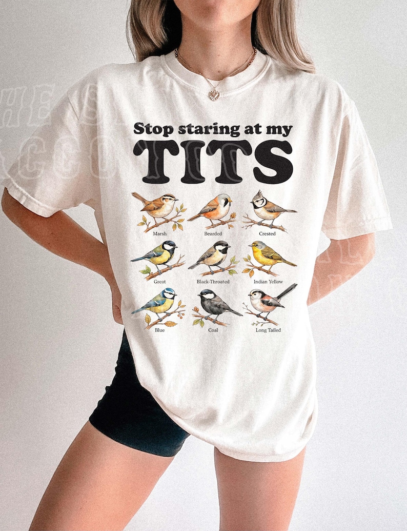 A person wearing a white t-shirt with a graphic design of various bird species and the text "Stop staring at my TITS" printed on it.